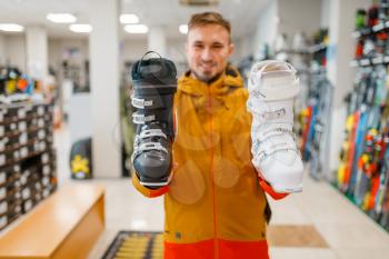Man shows white and black ski or snowboarding boots in sports shop. Winter season extreme lifestyle, active leisure, male customer with protect equipment