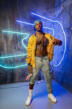 Black rapper in underpass neon light on background. Rap performer in club with grunge walls, underground music concert, urban style