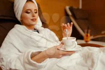 Sexy girl in bathrobe and towel on the head relaxing with cup of coffee in spa chair. Relaxation leisure, healthy lifestyle, attractive woman resting in armchair, beauty salon