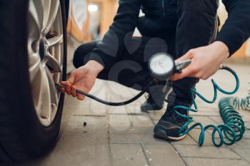 Male person checks the tire pressure, tyre service. Vehicle repair service or business, man inflates the wheels on automobile outdoor