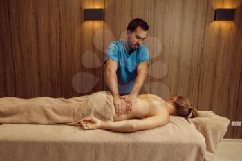 Male masseur rubbing back to slim woman with his elbow, professional massage. Massaging and relaxation, body and skin care. Attractive lady in a spa salon