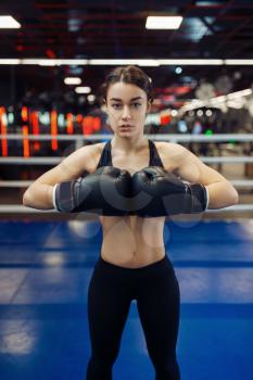 Woman in black boxing gloves holds out her hands, front view, box training in the ring. Female boxer in gym, girl kickboxer in sport club, punches practice