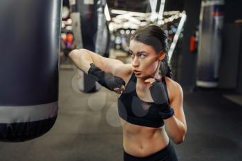 Woman in black bandages and sportswear hits a punching bag, thai boxing training. Female boxer in gym, girl fighter in sport club, elbow punches practice