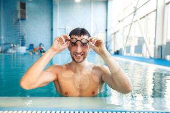 Male swimmer in swimming glasses poses in pool. The man at the poolside, aqua aerobics instructor poses in the water