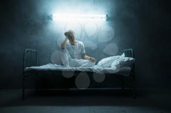 Psycho man sitting in bed, dark room on background. Psychedelic person having problems every night, depression and stress, sadness, psychiatry hospital