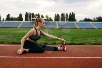 Female runner in sportswear, training on stadium. Woman doing stretching exercise before running on outdoor arena