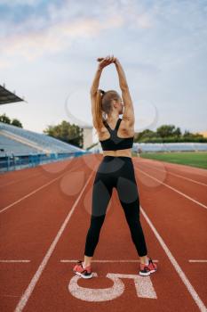 Female jogger in sportswear, training on stadium. Woman doing stretching exercise before running on outdoor arena