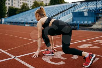 Female runner in sportswear on start line, training on stadium. Woman doing stretching exercise before running on sports arena