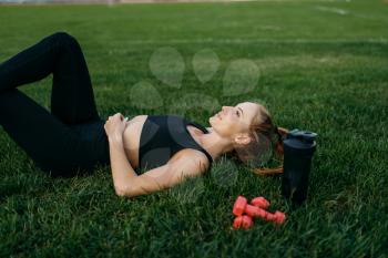Female runner in sportswear lying on the grass, top view, workout on stadium. Woman doing stretching exercise before running on outdoor arena