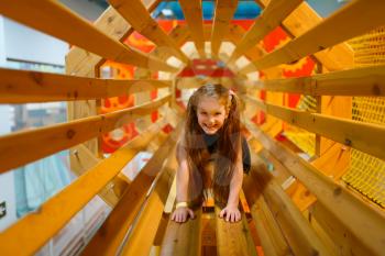 Little girl playing in wooden labyrinth, playground in entertainment center. Play area indoors, playroom