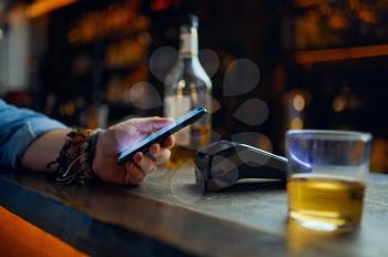 Man pays by phone at the bar counter, contactless payment. Male person puts the smartphone to the terminal in pub, modern safe technologies