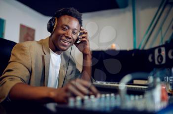 Happy male dj in headphones, recording studio interior on background. Synthesizer and audio mixer, musician workplace, creative process
