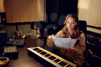 Female sound engineer in headphones, recording studio interior on background. Synthesizer and audio mixer, musician workplace, creative process