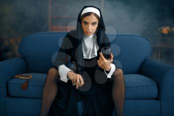 Sexy nun in a cassock with cigare and glass of wine sitting spreading her legs, front view, vicious desires. Corrupt sister in the monastery, sinful religious people, attractive sinner