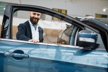 Man at the opened door of new automobile in car dealership. Customer in vehicle showroom, male person buying transport, auto dealer business