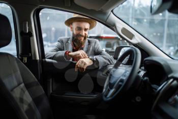 Man in cowboy hat looks interior of new automobile in car dealership. Customer in vehicle showroom, male person buying transport, auto dealer business
