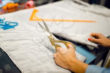 Seamstress cuts fabric with scissors in textile workshop. Woman works with cloth for sewing, female tailor at workplace