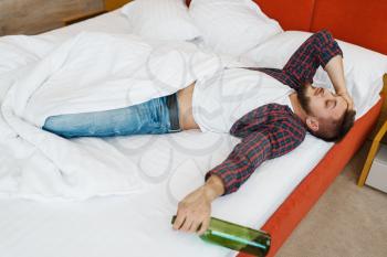 Drunken man sleeps in bed with bottle of wine. Male person with alcohol hangover, headache and depression, bad morning