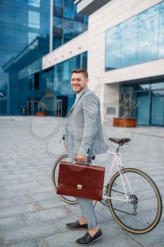 One businessman in suit with briefcase cycling in downtown. Business person riding on eco transport on city street
