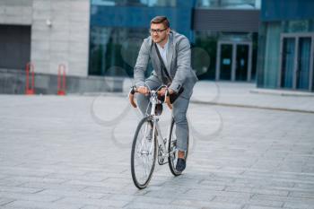 One businessman poses on bicycle at the office building in downtown. Business person riding on eco transport on city street