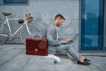 Businessman with bike and laptop having lunch at the office building in downtown. Business person riding on eco transport on city street, urban style