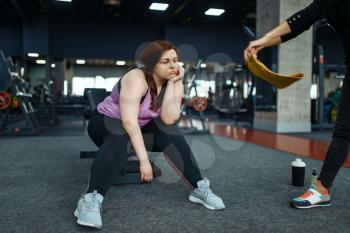 Tired overweight woman with trainer in sport club, fitness training with instructor. Female person struggles with excess weight, aerobic workout against obesity, gym