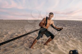 Muscular man doing exercise with rope in desert at sunny day. Strong motivation in sport, strength outdoor training