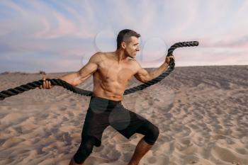 Muscular man doing exercise with rope in desert at sunny day. Strong motivation in sport, strength outdoor training