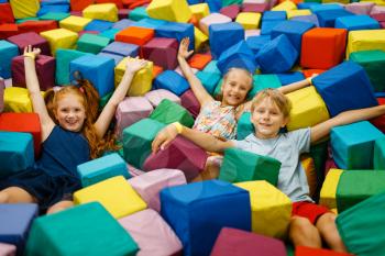 Happy children lying in soft cubes, playground in entertainment center. Play area indoors, play room