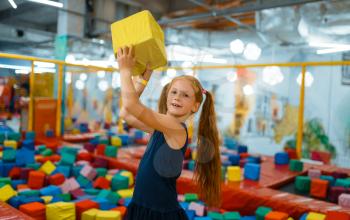 Adorable little girl playing with soft cube, playground in entertainment center. Play area indoors, playroom