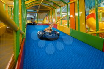 Little girl rides on tubing, playground in entertainment center. Play area indoors, playroom