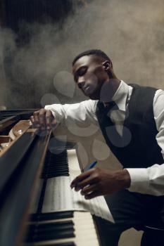 Black grand piano musician poses on the stage with spotlights on background. Negro pianist poses at musical instrument before concert