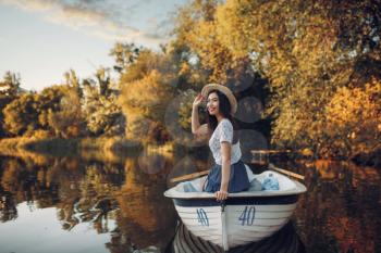Pretty lady poses in boat on quiet lake at summer day. Romantic date, boating trip, man and woman walking along the river
