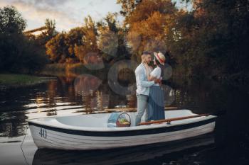 Lovers hugs in a boat on quiet lake at summer day. Romantic meeting, boating trip, man and woman walking along the river
