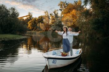 Love couple standing in a boat on quiet lake at summer day on sunset. Romantic meeting, boating trip, man and woman walking along the river