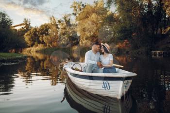 Love couple with fruit basket, relaxing in boat on quiet lake at summer day. Romantic date, boating trip, man and woman walking along the river