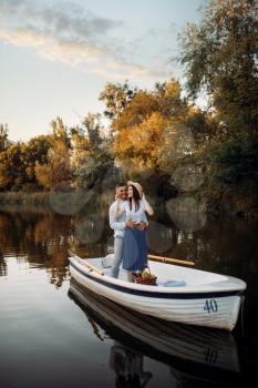 Love couple standing in a boat on quiet lake at summer day on sunset. Romantic meeting, boating trip, man and woman walking along the lake