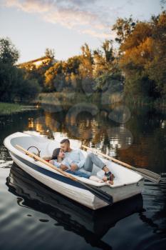 Love couple lying in a boat on quiet lake at summer day at sunset. Romantic meeting, boating trip, man and woman walking along the river