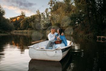 Love couple hugs in a boat on quiet lake at sunset. Romantic meeting, boating trip, man and woman walking along the river