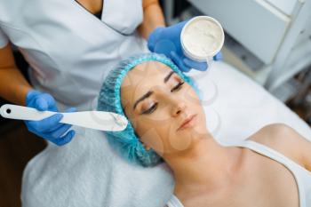 Cosmetician applies the cream to female patient's face, botox preparation. Rejuvenation procedure in beautician salon. Doctor and woman, cosmetic surgery against wrinkles and aging