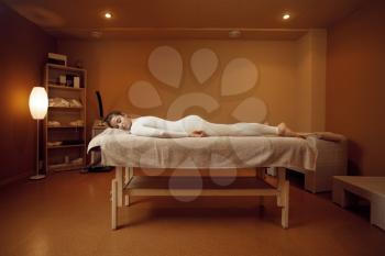 Young woman in massage suit relaxing on the table. Massaging and relaxation, body and skin care. Female person lying down in spa salon