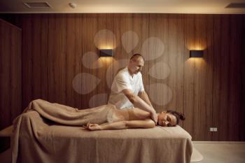 Male masseur pampering neck to young woman in towel, professional massage. Massaging and relaxation, body and skin care. Attractive lady in spa salon