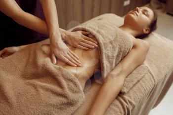 Female masseur pampering the stomach to young woman in towel, professional massage. Massaging and relaxation, body and skin care. Attractive lady in spa salon