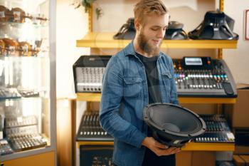 Bearded young musician buying subwoofer speaker in music store. Assortment in musical instrument shop, male musician choosing keyboard