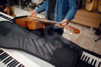 Male guitarist puts acoustic guitar in the case in music store. Assortment in musical instruments shop, musician buying equipment