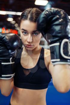 Woman in black boxing gloves in the ring, closeup front view, box training. Female boxer in gym, girl kickboxer in sport club, punches practice