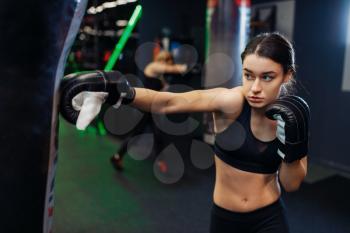 Woman in black boxing bandages and sportswear hits a punching bag, box training. Female boxer in gym, girl kickboxer in sport club, punches practice