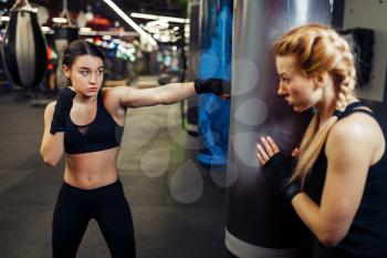 Woman in boxing bandages hits a punching bag, box training with trainer. Female boxers in gym, kickboxing workout in sport club, punches practice