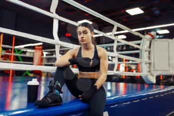 Woman in black boxing bandages sitting at the ropes on the ring, box training. Female boxer in gym, girl kickboxer in sport club, kickboxing workout