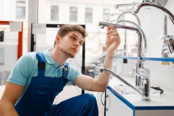 Plumber in uniform at showcase in plumbering store. Man with notebook buying sanitary engineering in shop, water taps and faucets choice